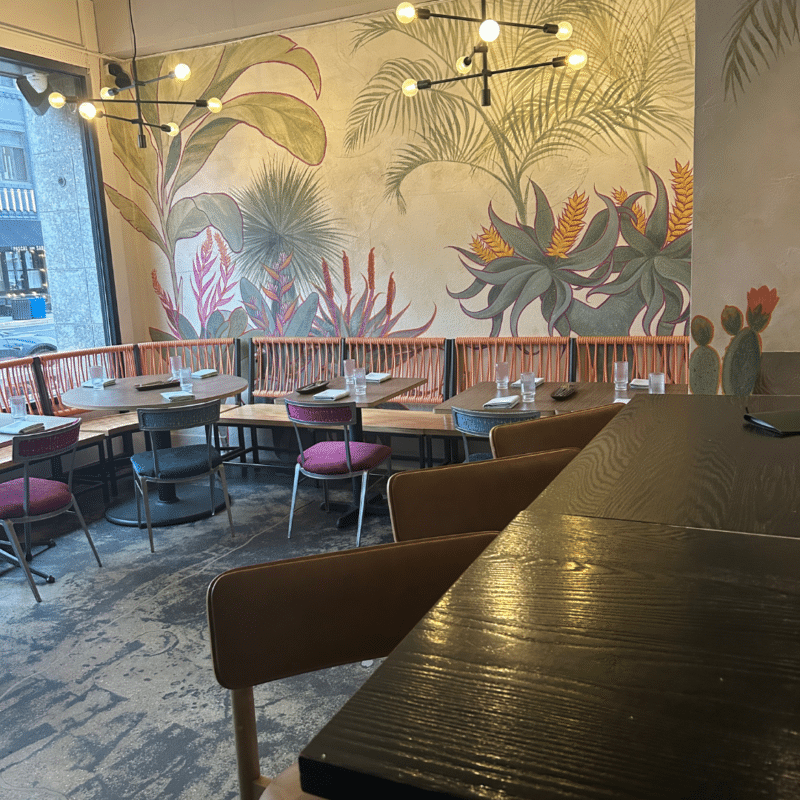 Dining room at Barrio Costero with tables, chairs, and a plant-themed wall mural