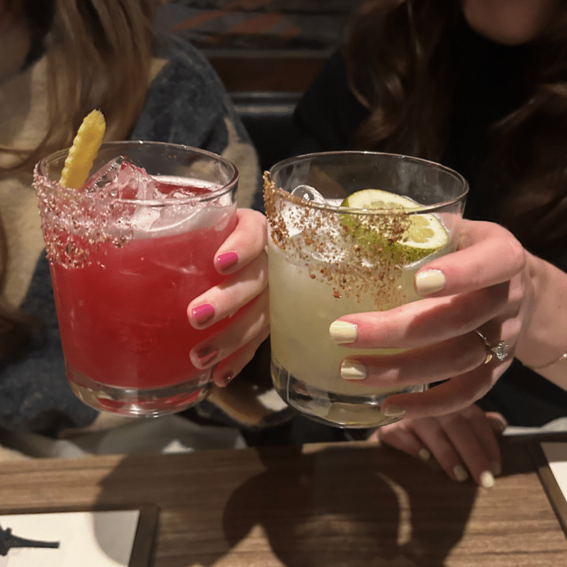 Two hands holding a red margarita and a lime green margarita