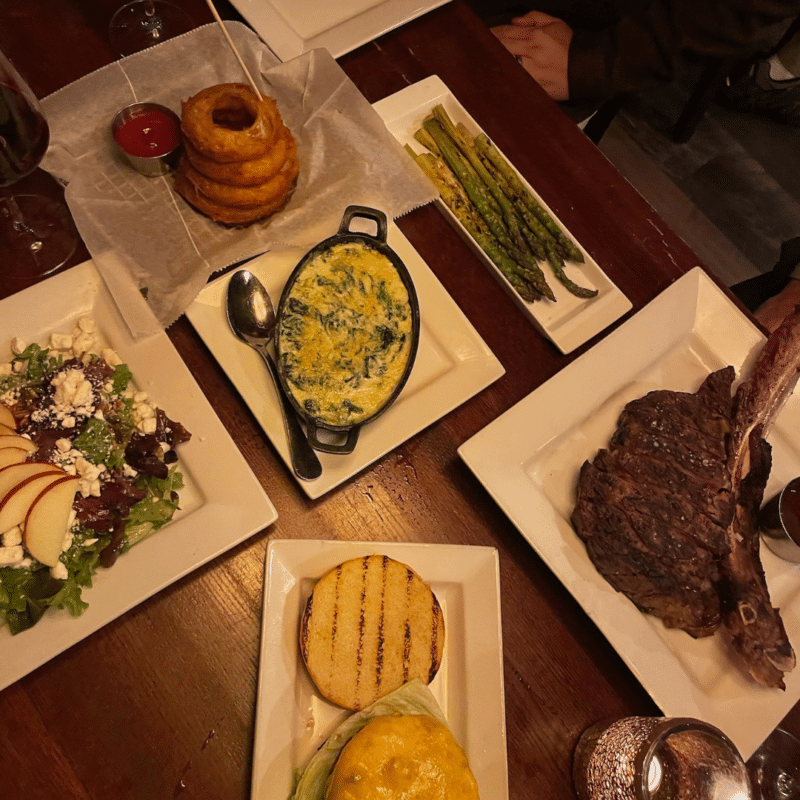 Spread of food at Sinner's Steakhouse including steak, onion rings, and a salad