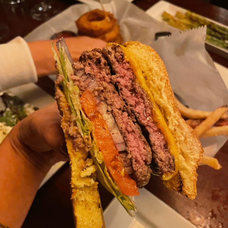 Hand holding a burger with onion rings and fries in background